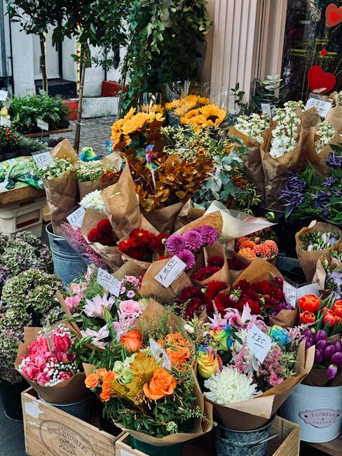 A vibrant display of freshly arranged flower bouquets outside a florist shop, featuring a variety of colours and flower types. Prominent yellow sunflowers, white lilies, and purple irises are wrapped 